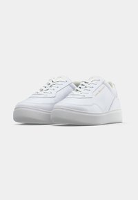 Ein Paar weiße Low-Top-Sneaker mit dicken Sohlen und dem goldenen "Tommy Hilfiger"-Logo an der Seite und Zunge.