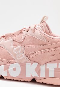 Baskets roses avec des accents en daim et cuir patent, arborant un grand logo blanc "HELLO KITTY" et un détail en forme de nœud sur le côté.