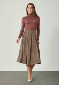 Jupe midi plissée marron associée à un col roulé ajusté mauve. La jupe a un tissu texturé et se porte à la taille. Portée avec des talons clairs.