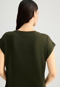 T-shirt verde oliva con scollo rotondo e maniche corte arrotolate, realizzato in un tessuto morbido, caratterizzato da una vestibilità comoda e una texture liscia.
