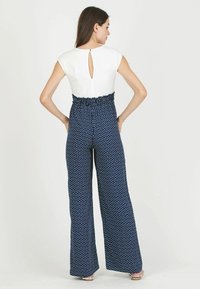 Jumpsuit à pois bleu marine avec une taille smockée ajustée, des manches courtes et un détail dans le dos en forme de trou de serrure, avec un pantalon style wide-leg.