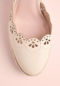 Light beige espadrille with cut-out floral pattern along the scalloped edge. Features a soft lining and natural jute sole. Smooth leather surface.