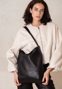 Zwarte leren schoudertas met een gestructureerde afwerking en een gladde onderpaneel, met een gebogen open bovenkant en een lange schouderriem.