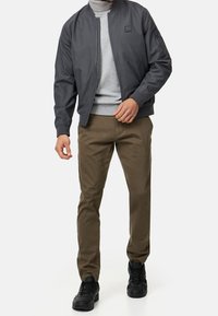 Grijze bomberjack, grijze coltrui, olijfkleurige chino's, zwarte sneakers. Gladde stof, ribbelmanchetten, ritssluiting aan de voorkant, zijzakken, minimalistische branding.