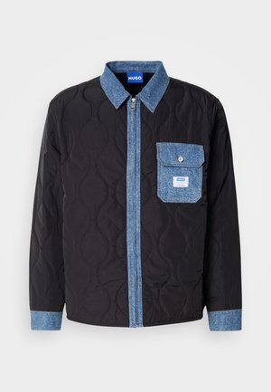 Zwarte gewatteerde jas met denimaccenten, voorzien van een ritssluiting aan de voorkant, een puntkraag en een borstzak. Het ontwerp combineert gestructureerde materialen.