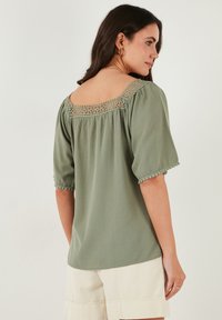 Green, lightweight blouse with short, puffed sleeves. Features a lace trim along the neckline and hem. Smooth texture with relaxed fit.