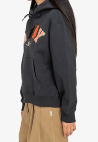 Sweat-shirt à capuche noir avec des broderies colorées portant l'inscription "PLAY," doté d'une poche kangourou et de poignets côtelés. Tissu doux et texturé.