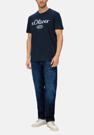 Dunkelblauses Baumwoll-T-Shirt mit weißem "s.Oliver"-Logo und Text. Kombiniert mit dunkelblauen Jeans und weißen Turnschuhen. Schlichte, klassische Passform.