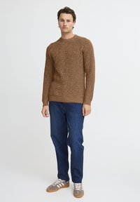 Brun strikket sweater med en tekstureret finish, parret med blå jeans og grå sneakers med hvide striber og snørebånd.