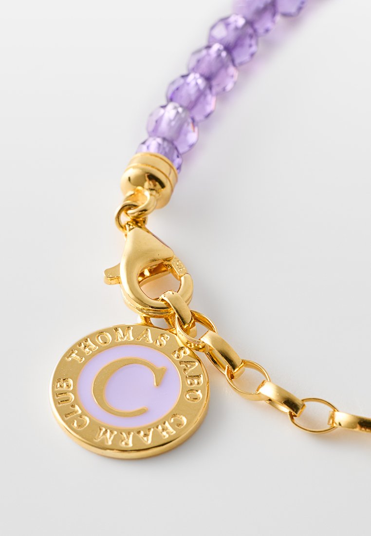 Lila Perlenarmband mit goldfarbener Metallschließe und -beschlägen, mit einem runden Anhänger, der mit "THOMAS SABO" und einem "C." graviert ist.
