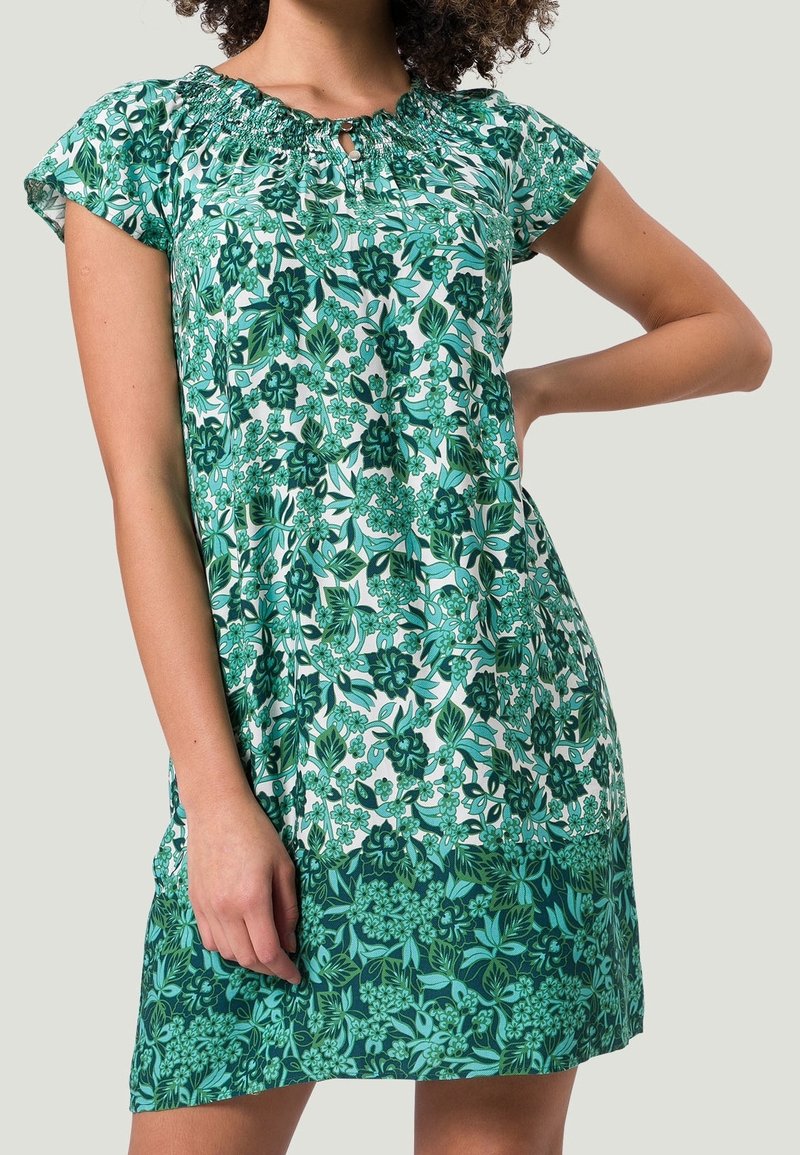 Robe courte florale verte avec des manches courtes, décolleté froncé et un design fluide. Présente des nuances variées de vert et des motifs complexes.