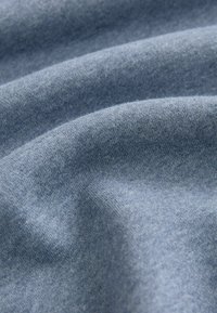 Tessuto blu con una texture liscia, caratterizzato da sottili variazioni di tonalità e una finitura morbida, leggermente opaca. Nessun motivo o accessorio visibile.