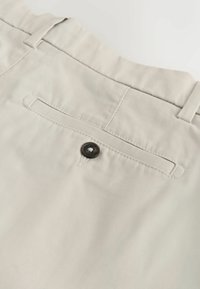 Poche arrière beige du pantalon avec un seul bouton foncé, passants de ceinture et coutures visibles sur tissu lisse.