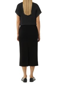 Czarny top z krótkimi rękawami zestawiony z czarną, dopasowaną midi spódnicą. Modelka nosi czarne płaskie buty. Minimalistyczny design bez wzorów.