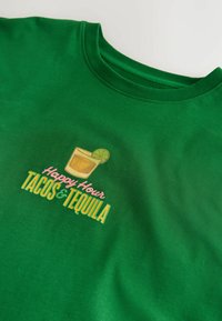 T-shirt vert avec un dessin d’un verre de tequila avec citron vert et le texte « Happy Hour TACOS & TEQUILA » en rose, jaune et vert.