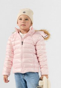Giacca a vento rosa con finitura lucida, chiusura con zip e cappuccio con bordino di pelliccia. Jeans blu e berretto crema completano il look.