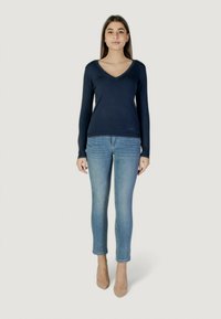 Pullover navy a V con maniche lunghe, abbinato a jeans skinny azzurri chiari. Tacchi beige completano l'outfit. Texture liscia in tutto.