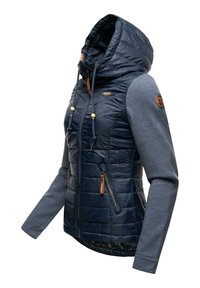 Marinblå huva jacka med quiltad framsida, dragkedjor, och grå långa ärmar med en rund läderpatch på vänster arm.