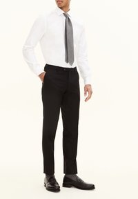 Männeroutfit mit einem weißen Hemd, einer grauen gemusterten Krawatte und schwarzen maßgeschneiderten Hosen, ergänzt durch schwarze Slipper und graue Socken.