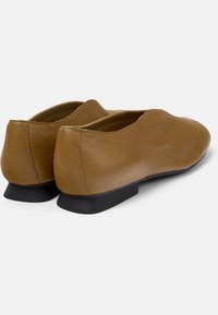 Zapatos planos de cuero marrón con punta redondeada, un tacón bajo negro y un acabado liso. Sin patrones visibles ni detalles metálicos.