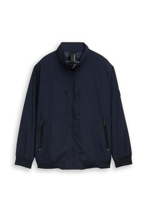 Marineblaue Reißverschlussjacke mit Stehkragen, zwei Brusttaschen mit Reißverschlüssen und zwei seitlichen Reißverschlusstaschen, flach auf weißem Hintergrund ausgelegt.