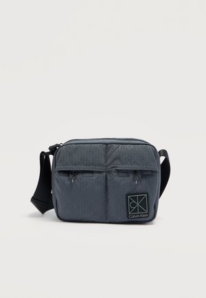 Szürke steppelt válltáska dupla cipzáras zsebekkel, fekete pánttal és Calvin Klein logóval az elején. Kompakt méret, sima textúra.