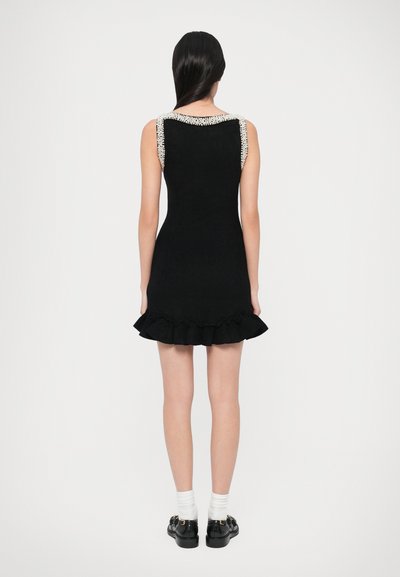 Svart klänning med utsvängd volangprydd fåll, ärmlös design och pärldetaljer på axlarna. Mjuk textur, knälång.
