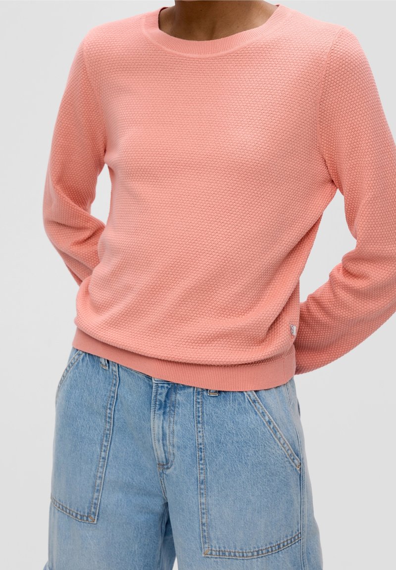 Pull rose clair texturé avec un col rond et des poignets côtelés, associé à un short en denim bleu taille haute.