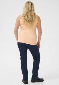 Peach sleeveless top with a textured finish, paired with dark blue denim jeans, featuring a straight leg design and black shoes.