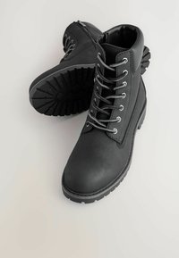 Ein Paar schwarze Leder Schnürstiefeletten mit robusten Gummisohlen auf einem hellen Hintergrund.