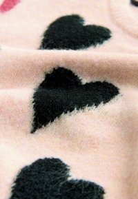 Rozā audums ar melnu sirdīšu rakstu, kas izceļ mīkstu, pūkainu tekstūru un omulīgu dizainu. Malas ir nedaudz izsistas.