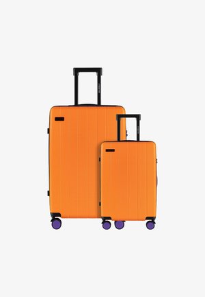 Twee oranje harde koffers, een grote en een kleine, met verticale ribbelstructuur, zwarte handvatten en paarse wielen.