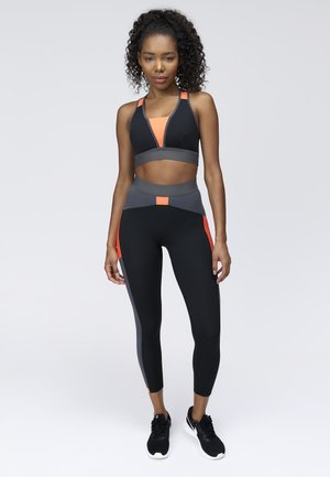 Black sports bra and leggings with orange and gray accents. The fabric is form-fitting with a smooth texture and contrasting color blocks.