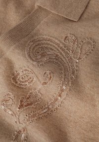 Tissu tricoté beige avec un motif floral, orné de paillettes en or rose brillant, créant un aspect texturé.