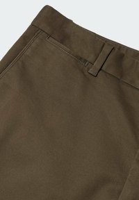 Gros plan d’un pantalon en tissu marron montrant la ceinture, la boucle de ceinture et les coutures de la poche avant.