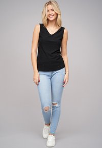 Zwarte mouwloze top met een V-hals en een gestructureerd patroon, gecombineerd met lichtblauwe ripped jeans en witte sneakers.