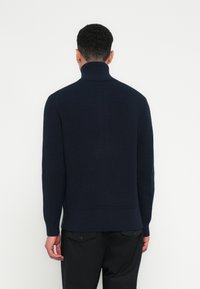 Mornarsko modra žametasta pulover s turtleneck ovratnikom in dolgimi rokavi, teksturirana tkanina in prilegajoča silhueta. Rob in manšete so imeli dodan žametni detajl.