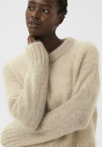 Pull tricoté ample beige clair avec un col côtelé et des manches texturées, fabriqué dans un matériau doux et duveteux.