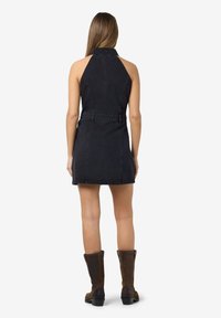 Zwarte denim halterjurk met een fitted taille en een korte zoom. Gestyled met bruine kniehoge laarzen. Gladde textuur, minimale details.