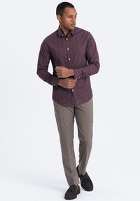 Bordeaux overhemd met knopen en een klein wit bloemenpatroon; lichtbruine geruite broek; donkere loafers; effen achtergrond.