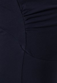 Tecido azul marinho com textura franzida, com áreas suaves e elásticas. O design inclui costuras curvas para um silhueta ajustada.