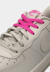Λευκό αθλητικό παπούτσι Nike Air Force 1 με φωτεινά ροζ κορδόνια και λογότυπο στη γλώσσα με σχέδιο λουλουδιού.