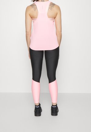 Débardeur de sport rose clair avec un design dos nageur, associé à un legging coloré en blocs noir et rose clair. Porté avec des chaussures de sport noires.