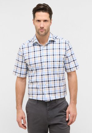 Mann trägt kurzärmeliges Hemd mit blauem, beige- und schwarzkariertem Muster und dunkelgraue Hose vor weißem Hintergrund.