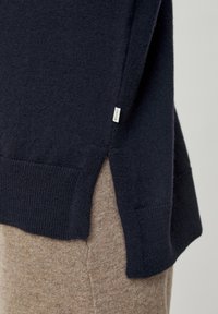 Marinsvett med en texturerad stickning. Sidoflikar avslöjar ljusbrun tyg under. Liten etikett på vänster söm. Ribbstickade manschetter och nederkant.