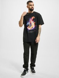 Sort t-shirt med et farverigt grafisk design med et kosmisk tema. Sammen med sorte cargo bukser og sorte sneakers.