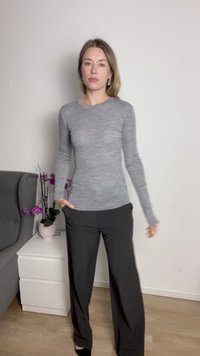 Szürke, hosszú ujjú, testhezálló felső, laza fekete nadrággal párosítva. Fekete cipők és egy rózsaszín növény egy cserépben látható.