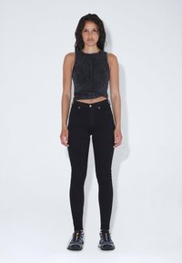 Top corto negro de ajuste ceñido con detalles de costura visibles, combinado con jeans ajustados negros de cintura alta y zapatillas deportivas negras.