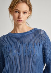 Zils adīts džemperis ar brīvu, atvērtu audumu un ribinātu apkakli. Satur tekstu "PEPEJEANS" kontrastējošā adījumā.