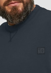 Granatowy sweatshirt z okrągłym dekoltem, wykonany z teksturowanej tkaniny, z małą czarną naszywką logo po lewej stronie. Miękki i trwały materiał.